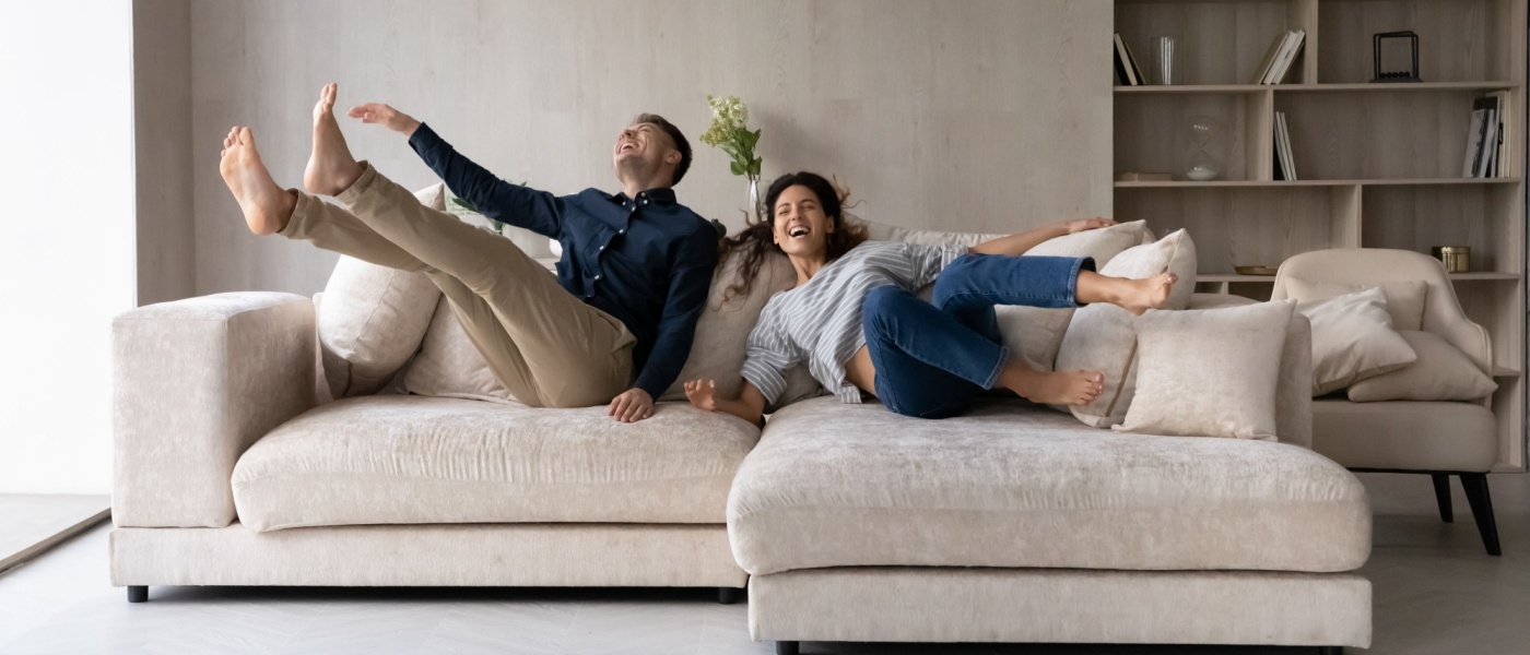 A happy couple relaxes and laughs on a cozy beige couch in their stylish apartment, embodying what makes a good renter—respectful, responsible, and enjoying their well-maintained living space.