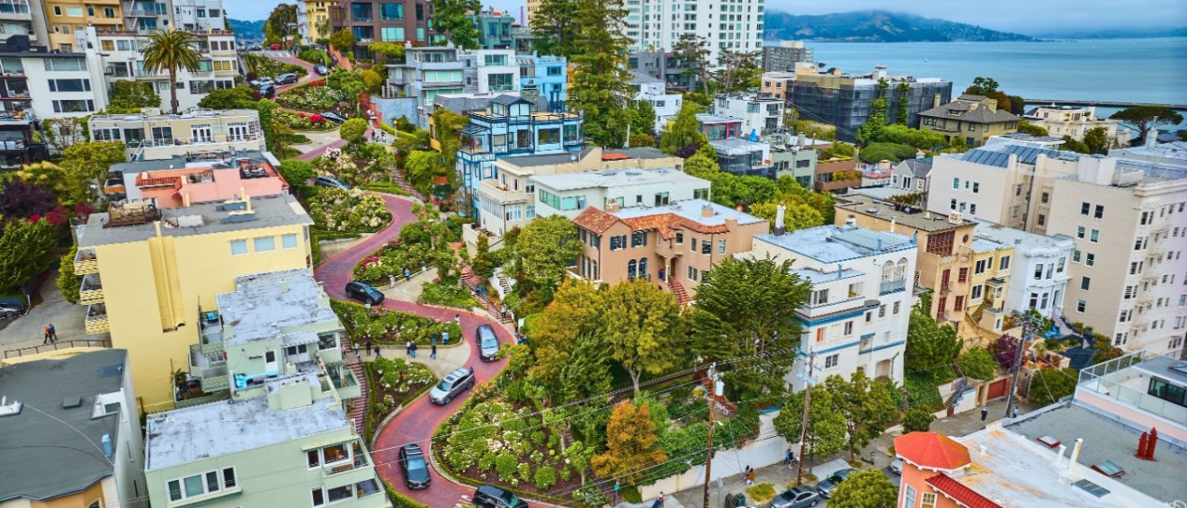 An aerial view of apartments in San Francisco along Lombard Street, showcasing colorful buildings, greenery and views of the nearby bay.