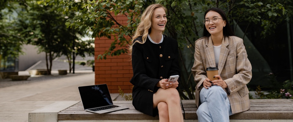Smiling young women standing outside on the street, casually dressed, talking and highlighting friendly interactions and how to ask questions for neighbors.