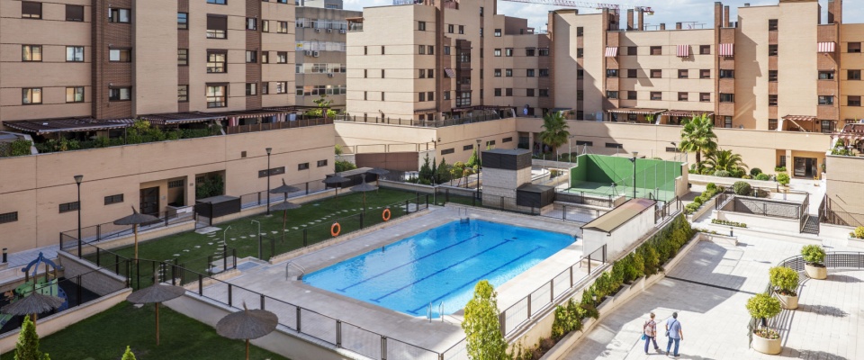 Common areas of an urbanization with swimming pools, benches, flower boxes, grassy lawns, and tennis courts, illustrating amenities maintained through common area maintenance fees.