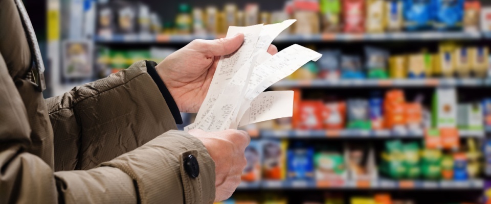 A person reviews receipts in a grocery store aisle, reflecting everyday expenses and the cost of living in Denver.