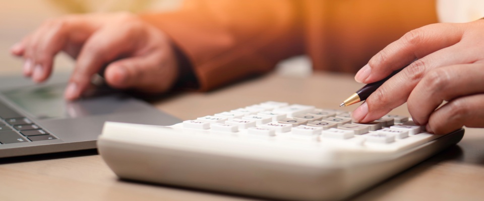 Financial accounting and business budgeting concept showing a professional using a calculator and laptop to manage expenses, illustrating finance management, audits, and the role of common area maintenance fees in budgeting.