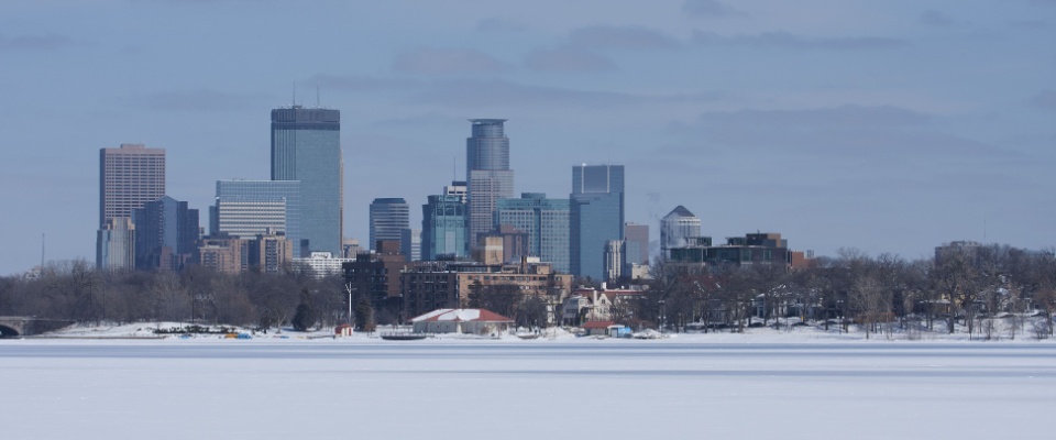 A waterfront view of Minneapolis in winter with the frozen-over lake.