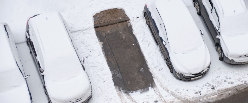 An aerial shot of a snowed-over parking lot in winter with a gap in the snow where a car had previously been parked.