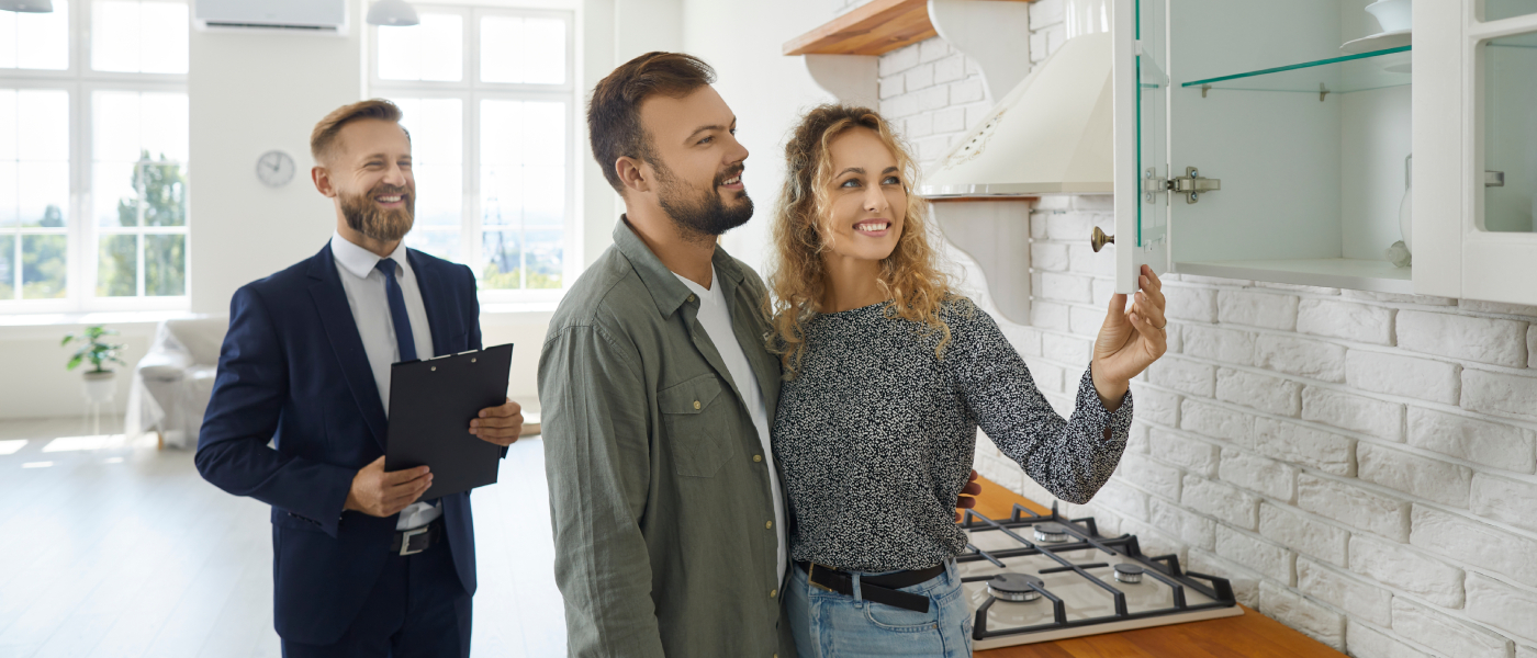 Couple inspecting kitchen cabinets during an apartment tour with a real estate agent, checking key details during peak rental season.