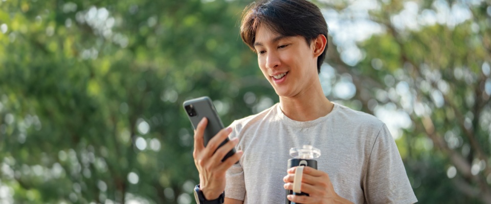 Man holding a mobile phone and bottle of water in a public park. He's using a smartphone to check great deals on rentals nearby.