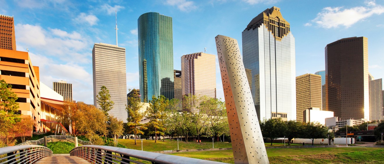 A shot of the skyline in Houston, as seen from a bridge in a park.