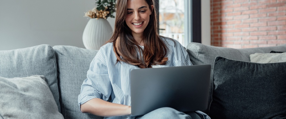 Concentrated woman sitting on the couch working on her laptop at home, searching for a great deal on a rental during a relaxed weekend.