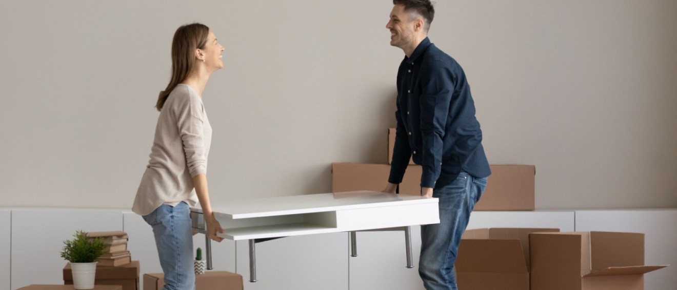 Two people lifting a white coffee table in a living room filled with moving boxes and packed belongings, illustrating the question how renters insurance covers moving.