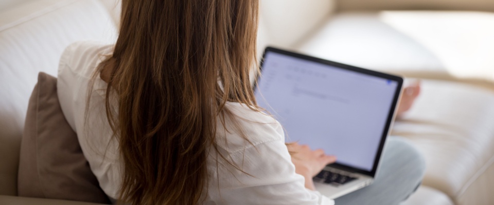 A woman sitting on a couch with a laptop, preparing a written notice to her insurance company as she researches how to cancel renters insurance.