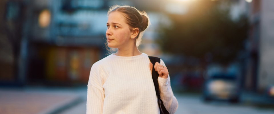 Young woman walking alone in a new city neighborhood, looking around while exploring after moving to a new state alone.