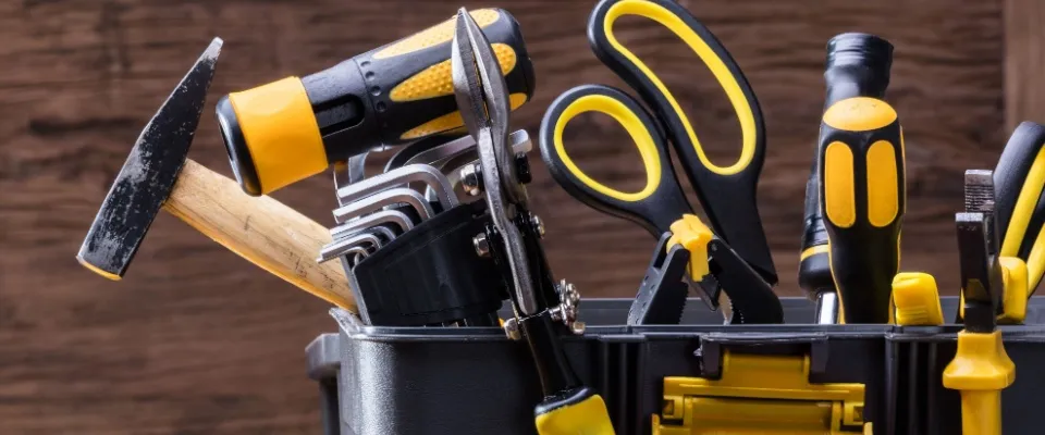 A close-up of a toolkit filled with essential tools like a hammer, screwdrivers, scissors, and pliers, useful in preventing emergency repairs in an apartment.