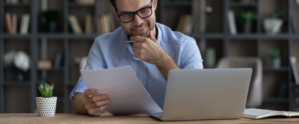 A person sits at a desk, thoughtfully reviewing a job application and using a laptop, conveying the importance of rent reporting and credit score for renters looking for more job opportunities.