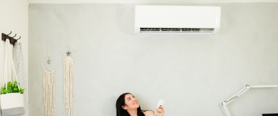 A smiling woman relaxes in her living room, enjoying the cool breeze from a mini split air conditioning unit on a hot summer day—one of the many comforts residents appreciate in well-equipped apartments in Atlanta.