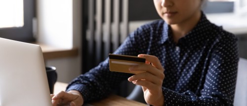 A close-up of a focused woman using her laptop and credit card to make a secure online payment, carefully managing finances and reviewing details related to an application fee.