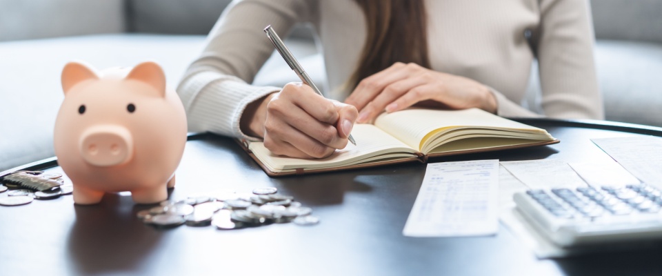 Young Asian businesswoman writing a budget by hand to manage expenses and save money, highlighting smart financial planning for the cost of living in Ann Arbor.
