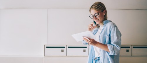 Smiling woman checking mail and talking on the phone in front of apartment mailboxes after changing her address.