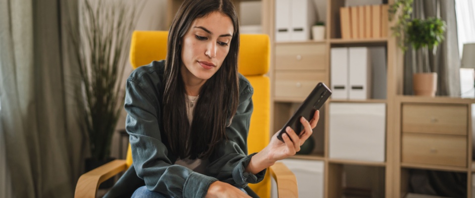 A worried adult woman uses her mobile phone to calculate household expenses, carefully budgeting while considering an application fee as part of her financial planning.