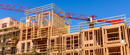 Wood-frame apartment buildings under construction with scaffolding and a red crane in the background