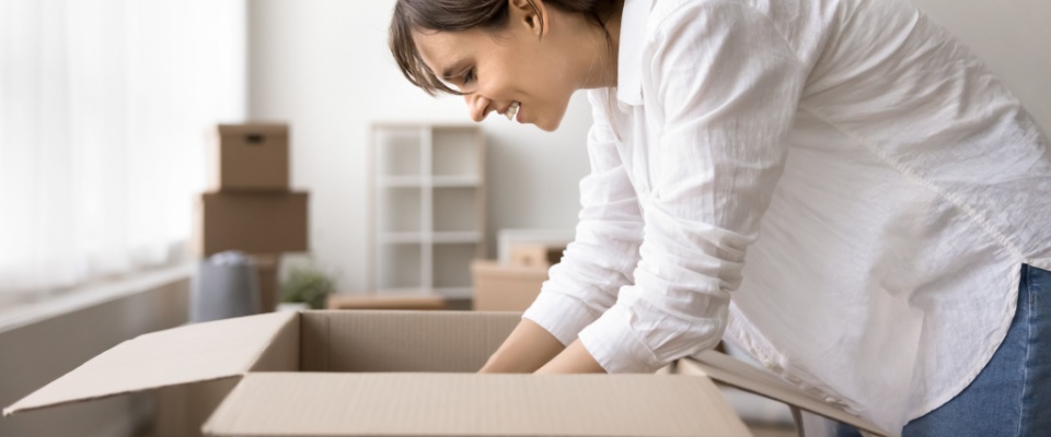 Young smiling woman unpacking belongings from cardboard boxes, symbolizing a fresh start after completing the move-out procedure.