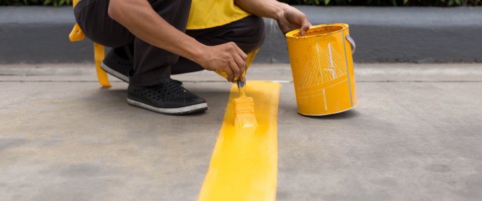 A worker painting a yellow line on the concrete floor of a car park — a clear example of how maintenance and organization are tied to parking questions in residential and commercial spaces.