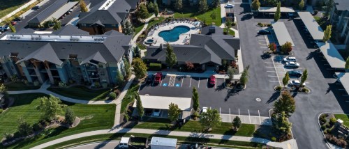An aerial view of an apartment complex pool beside a large empty lot raises practical parking questions, including availability, usage, and planning for residents and guests.