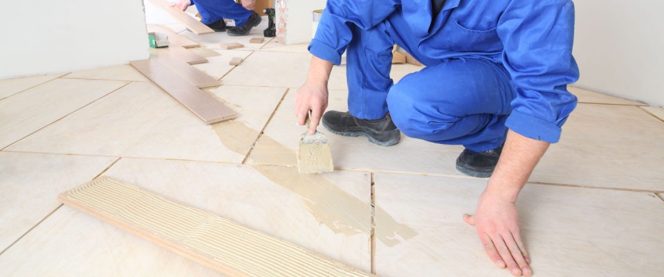 Two workers installing laminate flooring in a hallway highlight shared responsibility in common areas, ensuring durability and comfort for all residents.