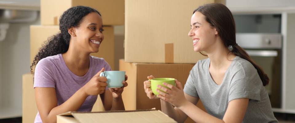 Two roommates relax and chat over drinks after a long day of unpacking — a common scene for those moving near a college town, where shared housing and new friendships often go hand in hand.