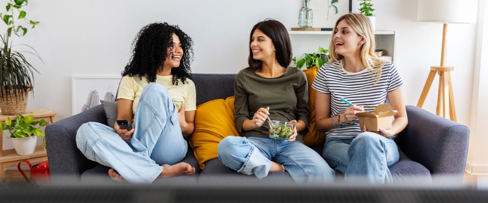 Three happy college students studying together on a laptop at home, showcasing the joy of friendship and shared living that comes with the search for a roommate.