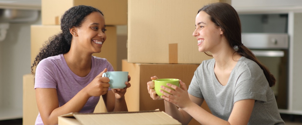 Two roommates relaxing together with drinks after moving, enjoying their new space and reflecting on the successful search for a roommate.