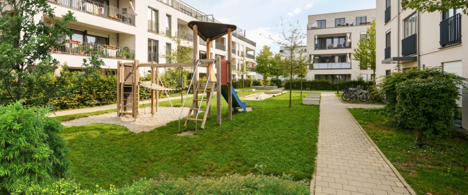 A cityscape with modern apartment buildings and green spaces reflects shared responsibility in common areas, where families benefit from sustainable urban living and well-maintained communal environments.