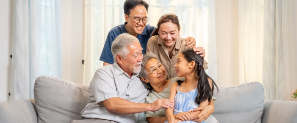 Three generations of a happy family relax together on the living room couch, enjoying weekend time and each other's company — a heartwarming example of connection in a multi-generational household.