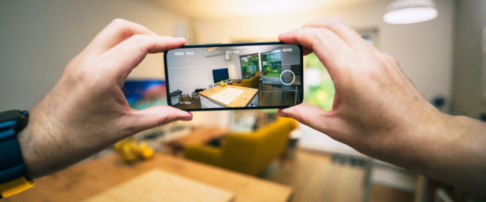 Hands holding a smartphone to capture photos of a home interior for a virtual tour, highlighting how technology supports real estate listings and the search for a roommate.
