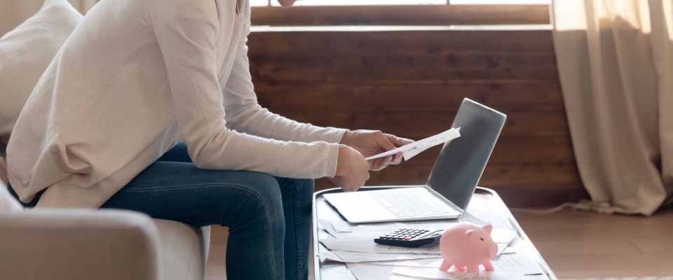 Side view of a young woman focused on financial documents at home, reviewing bills and rent payment terms, while considering the impact of an application fee on her monthly budget.