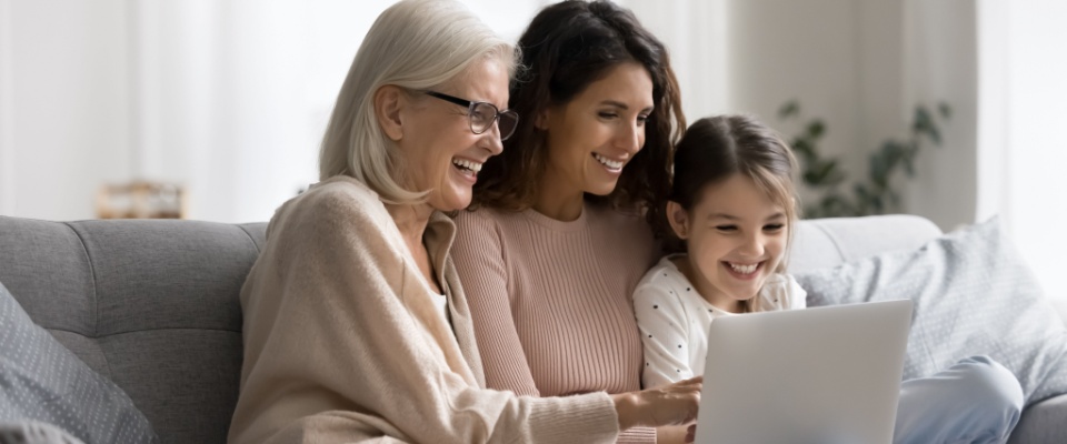 A joyful moment as a multigenerational family relaxes on the couch, enjoying a video call or online shopping together — a true glimpse into the harmony of a multi-generational household embracing technology.