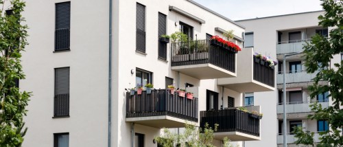 Modern apartment building featuring several balconies decorated with plants and flowers, illustrating principles of balcony etiquette by showcasing tidy, attractive outdoor spaces.