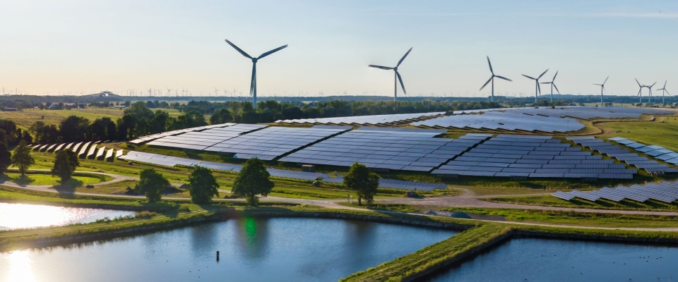 Expansive landscape featuring solar panels and wind turbines near a body of water, visually emphasizing the benefits of comparing electricity plans that offer renewable energy sources.