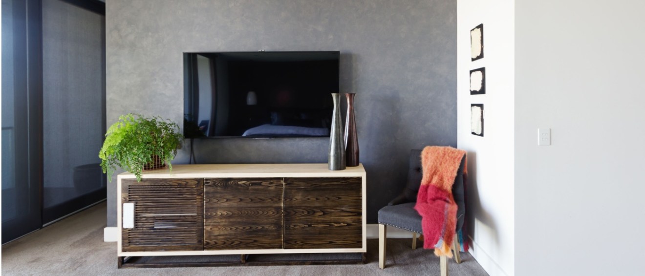 A modern living room with high-value items such as a large flat-screen TV mounted above a stylish wooden cabinet with decorative vases and a lush green plant.