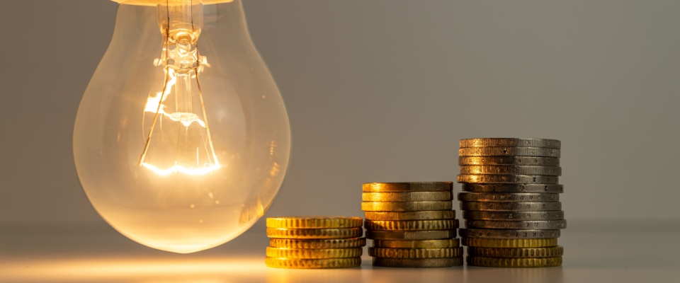 Illuminated light bulb next to stacked coins of varying heights, symbolizing the cost-saving benefits of comparing electricity plans to find the most affordable energy rates.