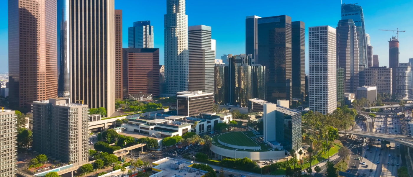 Aerial view of downtown Los Angeles with its skyline and streets under a clear blue sky. Scenes like this often spark conversations about finding affordable neighborhoods in a city known for its high cost of living.