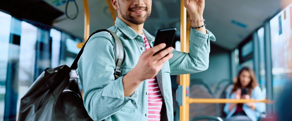 A happy man using a mobile app on his phone while riding a bus, showcasing the convenience and connected lifestyle available to residents of apartments in Las Vegas.