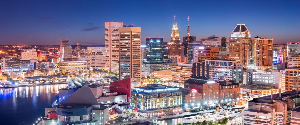 The Baltimore, MD skyline glows beautifully at dusk over the Inner Harbor, showcasing the vibrant city atmosphere and lifestyle available to those looking for apartments in Baltimore.