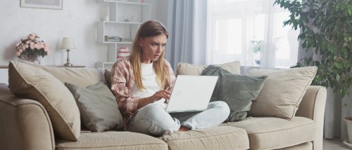 Stressed young woman sitting on a couch with her laptop, struggling during her apartment search, illustrating the challenges of reducing stress when apartment hunting.