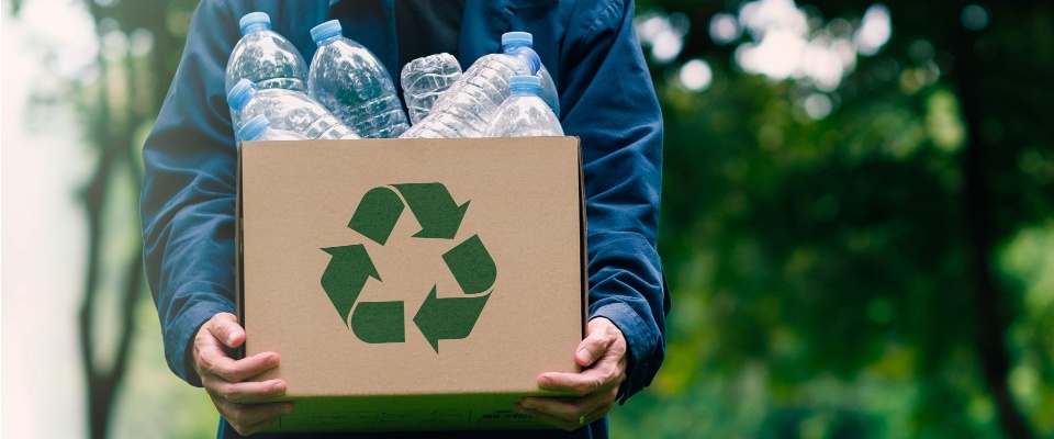 A businessman holding a cardboard box with a recycling symbol and water bottle, reflecting eco-friendly values and sustainable living often embraced in apartments in Las Vegas.
