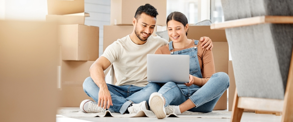 Happy couple sitting among moving boxes, researching rent inclusions online before renting apartments in Detroit.