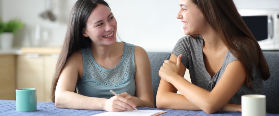 Two happy women discussing their living arrangement and responsibilities in the kitchen, reviewing details of their roommate agreement.