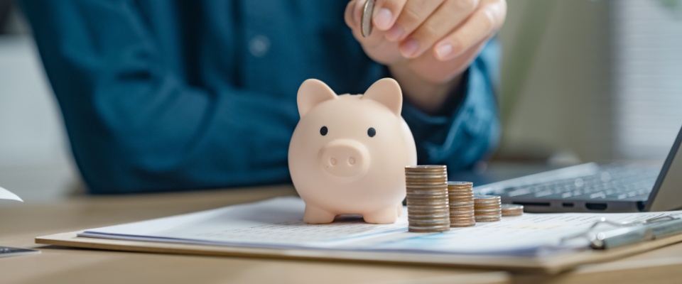 A person placing coins into a piggy bank, representing financial responsibility and planning for the future — a key part of managing expenses outlined in a roommate agreement.