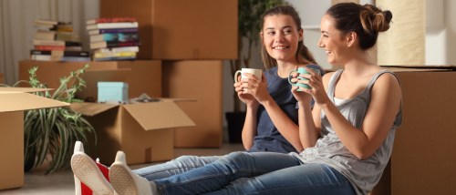 Two cheerful roommates relaxing on the floor after moving in together, discussing plans and expectations — a perfect time to create a roommate agreement for a smooth living arrangement.