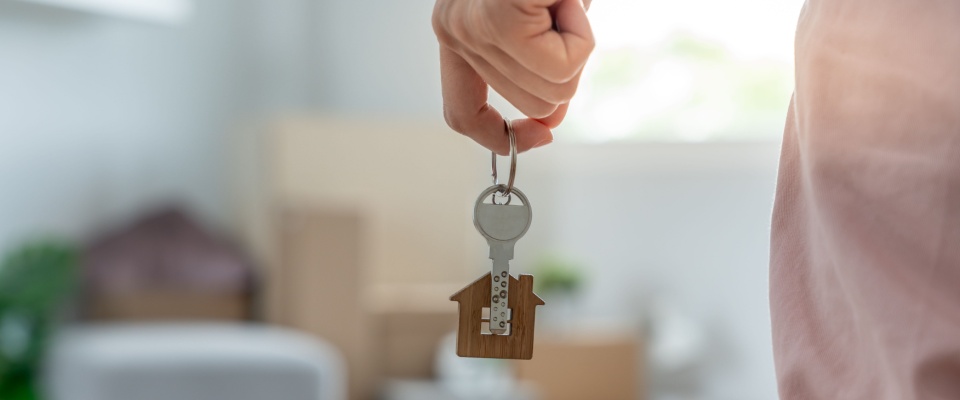 A woman holding a house keychain in her new apartment symbolizes moving into a new home. Moments like these often follow the signing of a lease, with the lease commencement date marking the official beginning of the rental period.