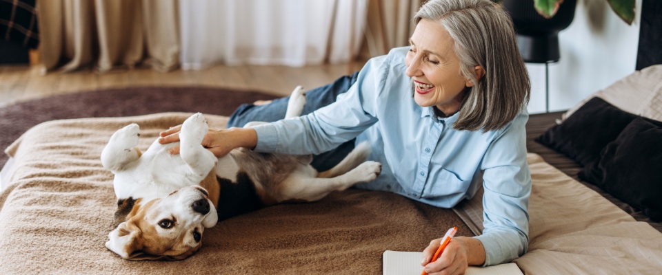 A happy retired woman lying on her bed, hugging her beagle while journaling — a cozy moment that also highlights the importance of planning for a pet deposit when renting with furry companions.